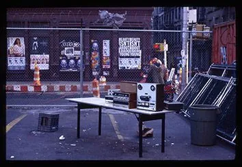 Sound equipment on a street table beside a fence covered in posters